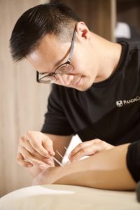 Acupuncturist placing needle into patient's arm during acupuncture session