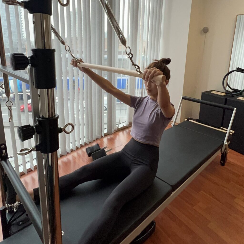 woman sitting on pilates reformer holding onto a workout bar