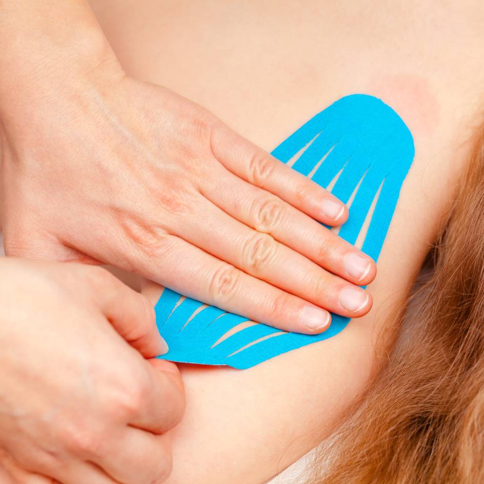 A close-up image of a person applying bright blue fascia tape to a woman's shoulder to help relieve pain and support muscle recovery. The tape is carefully placed to follow the natural lines of the muscles, commonly used in Fascial Stretch Therapy in Burnaby to enhance movement and reduce discomfort.