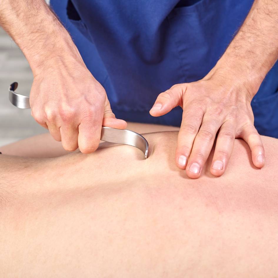 A close-up image of a therapist using a special curved tool to apply pressure on the back muscles of a client during a Fascial Stretch Therapy session in Burnaby. The therapist's hands skillfully manipulate the tool across the client’s back to help release muscle tension and enhance mobility in the rhomboid area.